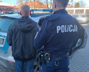 Dzielnicowy z zatrzymanym mężczyzną stoi obok radiowozu
