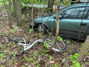 Uszkodzony rower i samochód marki Opel Astra leżące w przydrożnych zaroślach