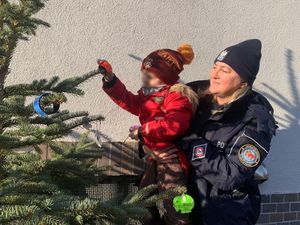 policjantka podsadza dziecko, które wiesza odblask