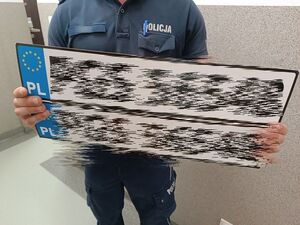 Policjant trzyma zabezpieczone podrobione tablice rejestracyjne